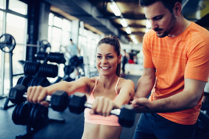 Frau trainiert mit Kurzhanteln und Personal Trainer